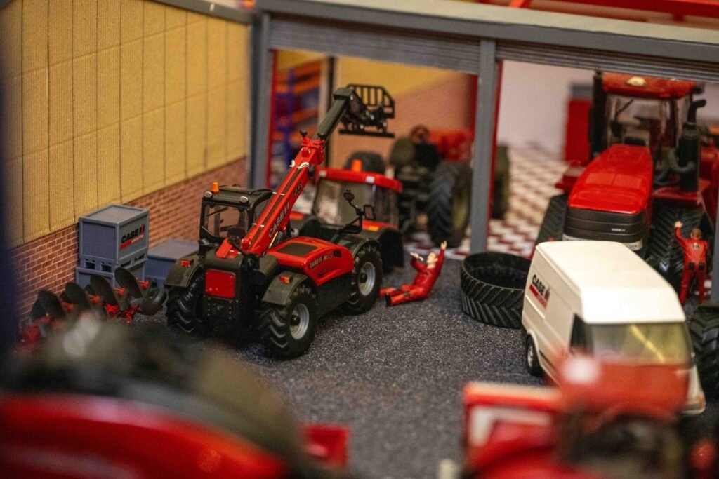 Model farm diorama showing miniature tractors and machinery parked outside a model farm building
