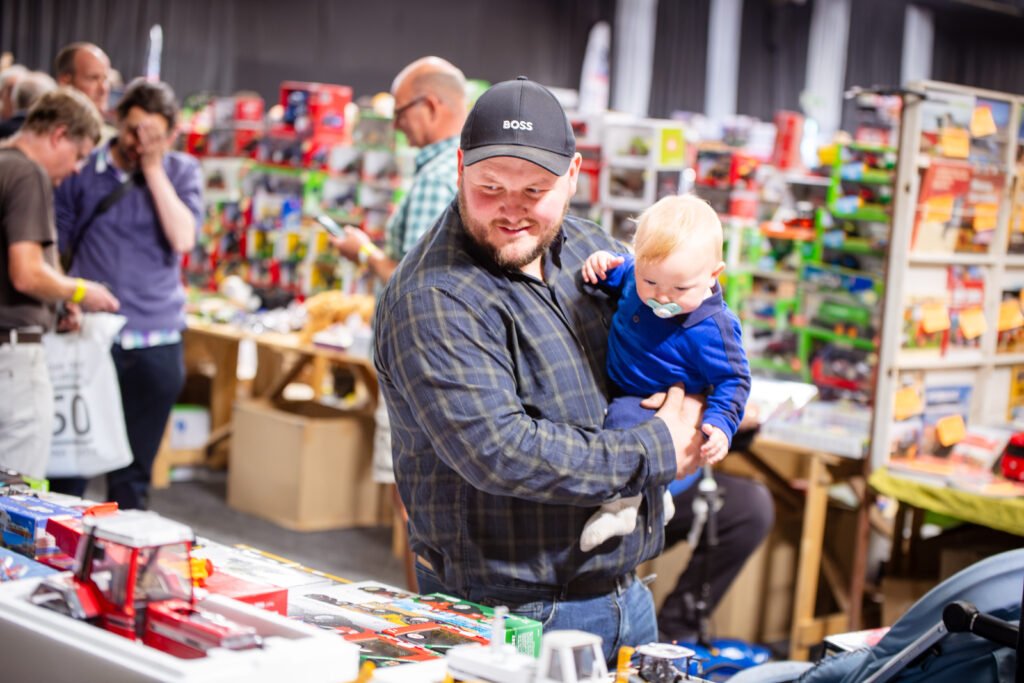 Visitor holding a small child while browsing a stand of model tractors