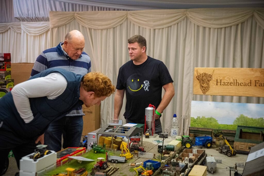 Traders talking with a visitor at a farm models stand